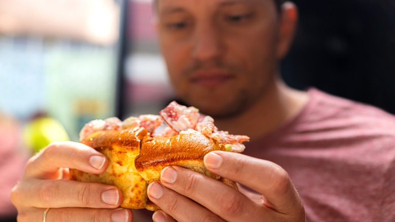 A young man holding up a lobster roll as he prepares to eat it