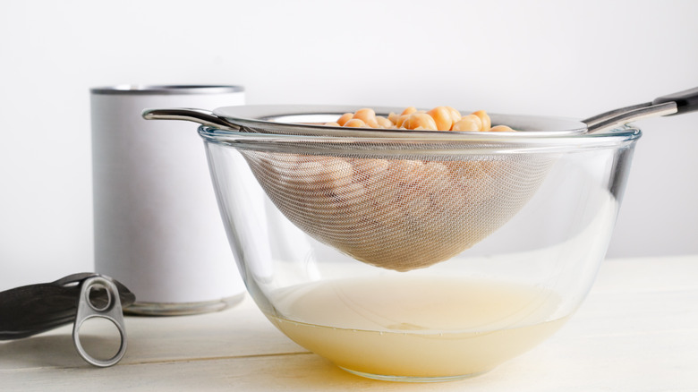 Chick peas in a sieve over a glass bowl with liquid