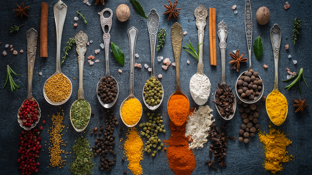 A variety of spices on spoons laying on a dark surfaces