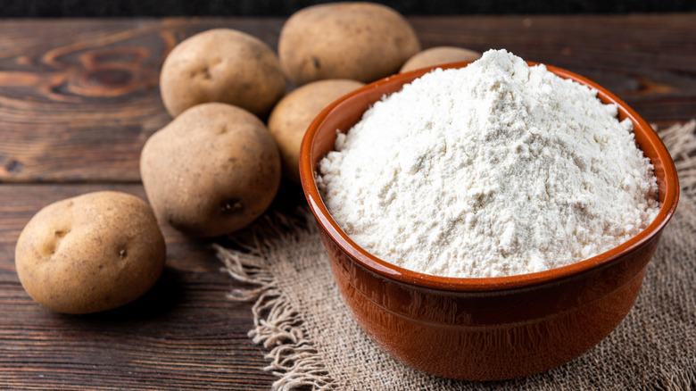 A bowl of potato flour next to potatoes