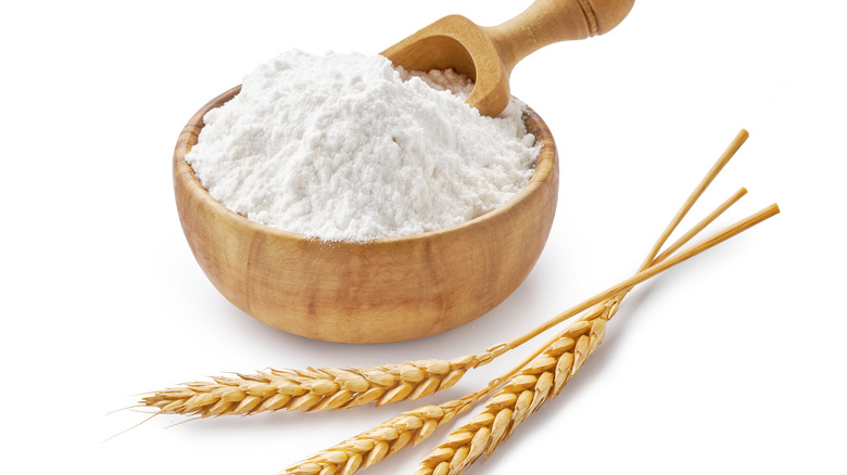 Wheat flour in a bowl with wheat grains next to the bowl