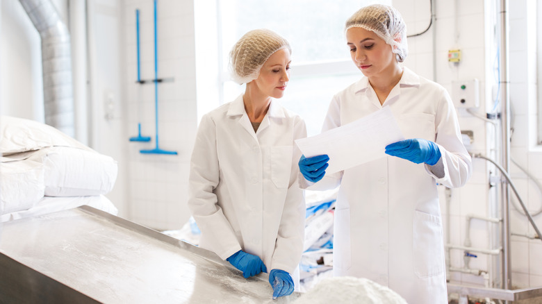 Two white women in hairnets and blue gloves working with powder