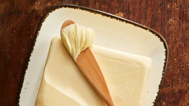 A pad of butter and wooden spoon on a rustic dish with a brown background