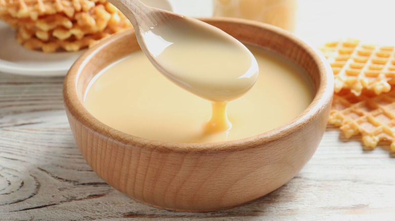 A wooden bowl of condensed milk with waffles in the background