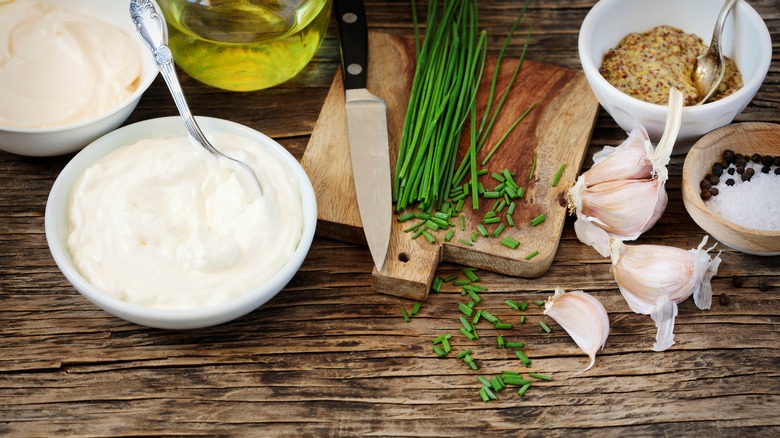 A bowl of sour cream next to savory ingredients like chives, garlic, and mustard