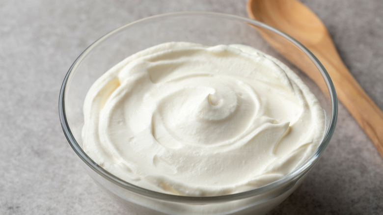 Plain crème fraîche in a bowl with a wooden spoon behind it