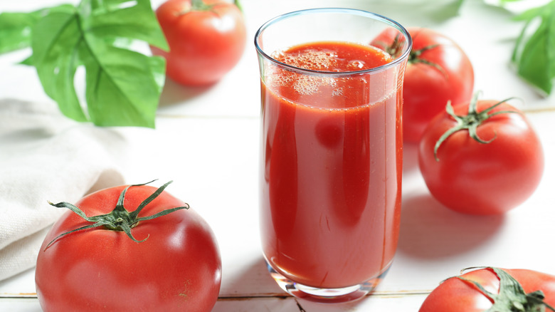 tomato juice in a glass surrounded by whole tomatoes