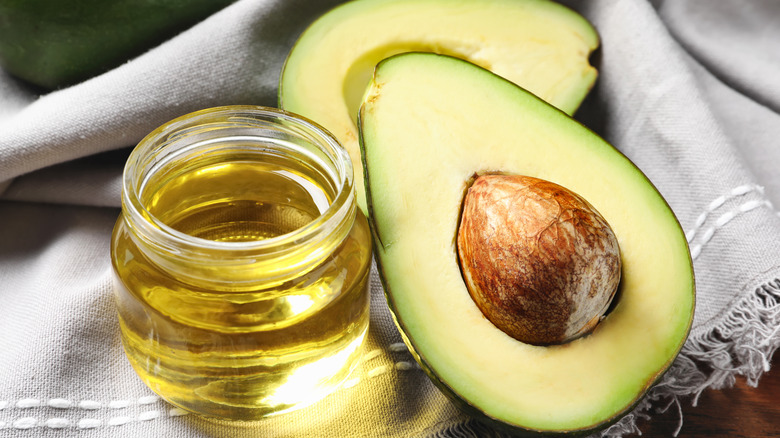 A sliced avocado next to a bowl of oil