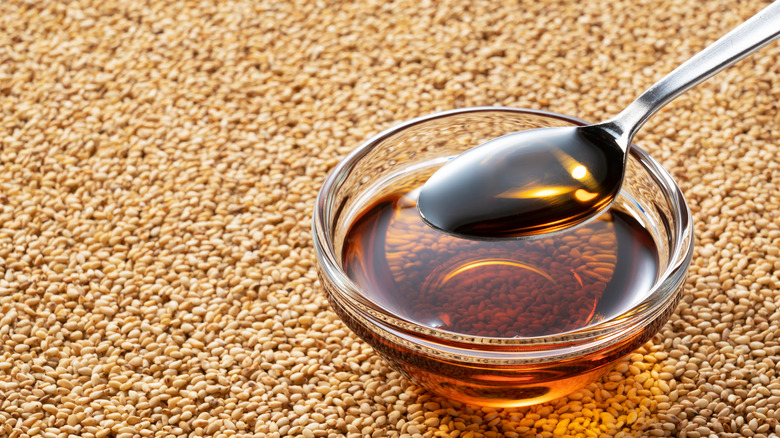 A bowl and spoon of sesame oil over sesame seeds