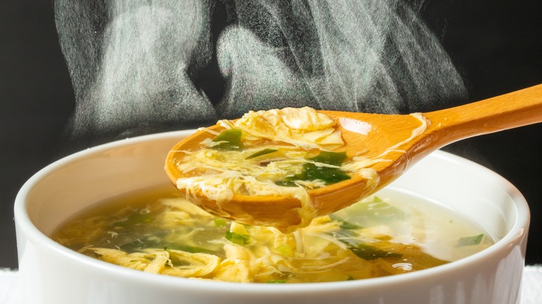 Egg drop soup in a white bowl with a wooden spoon