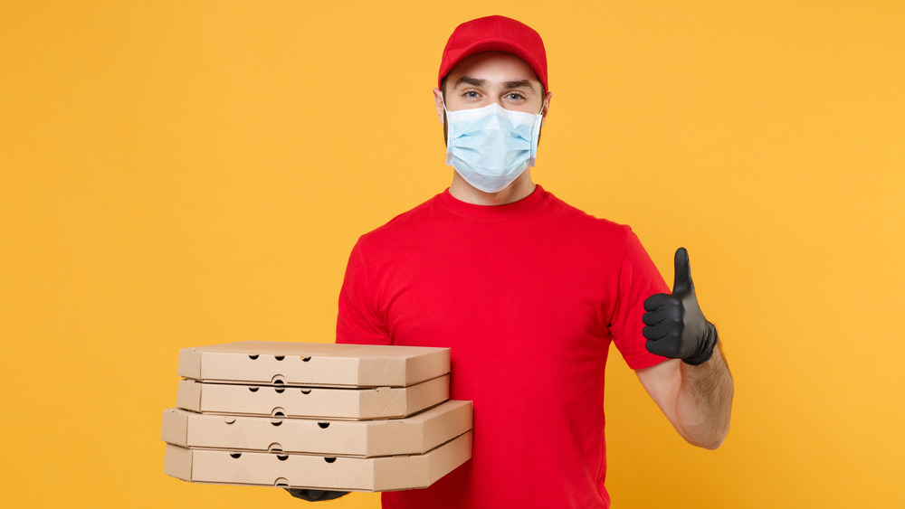 man in mask holding pizza boxes thumbs up