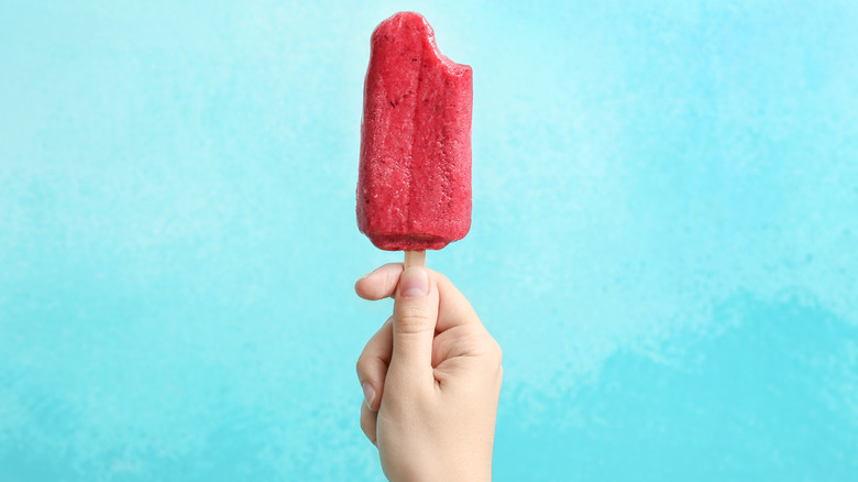 A woman holding a popsicle with bite taken out