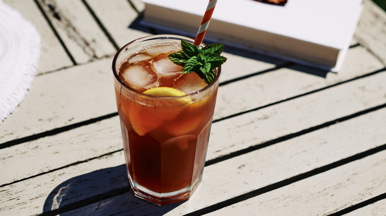 Glass of cloudy iced tea with ice cubes, lemon slice, garnish, and striped straw