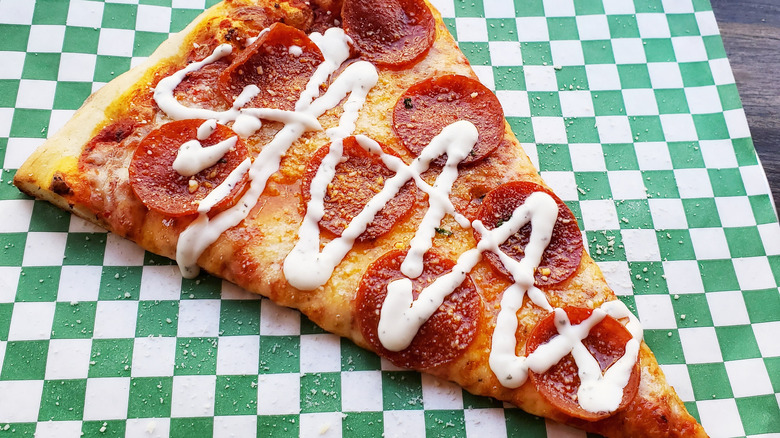 slice of pepperoni pizza with ranch drizzled on top.