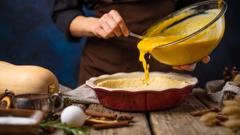 Person pouring custard filling into pie shell