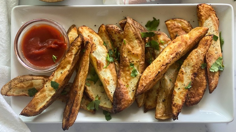 Steak fries on a plate with a small bowl of ketchup.