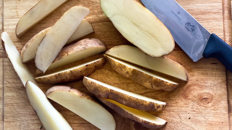 Sliced potatoes on a cutting board with a knife.