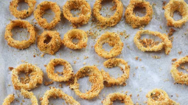 Coated onion rings on a lined baking tray.