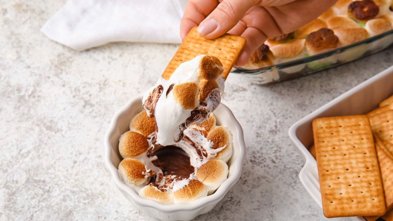 Hand dipping graham cracker in smore's dip