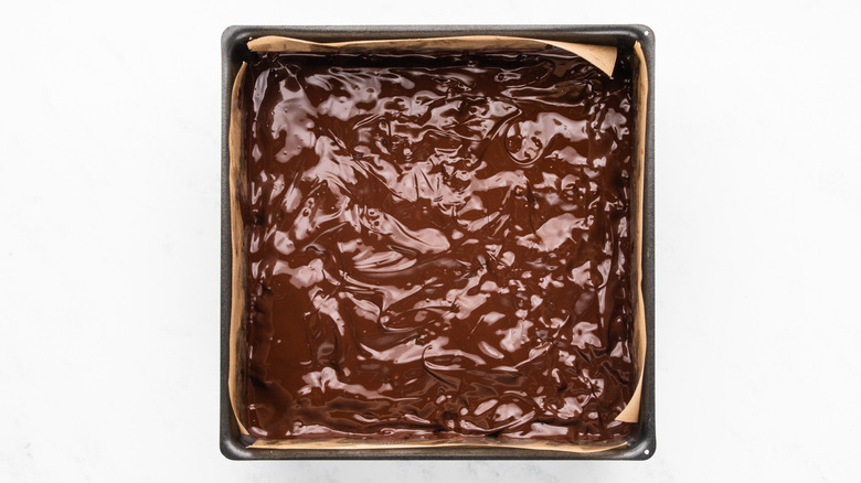 Melted chocolate on top of cereal bar slab in square baking tin