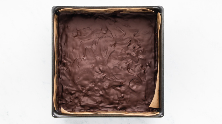 Chocolate-topped cereal bar slab in square baking tin