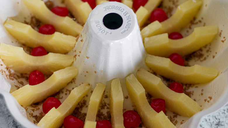 pineapple ring halves propped up in a bundt pan's grooves with cherries in between 