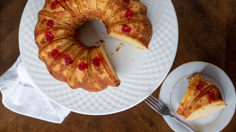 slice of homemade upside down pineapple cake from a bundt pan on a white plate with the cake nearby on a white plate