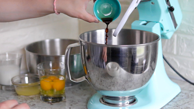 vanilla extract being poured into the stand mixer's bowl with eggs nearby