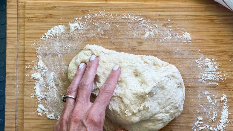 A hand kneading dough on a cutting board