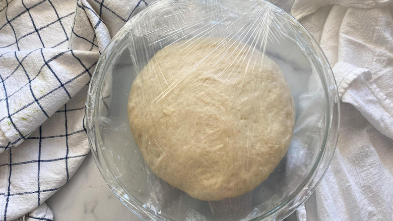 Dough sitting in a bowl with plastic wrap over it