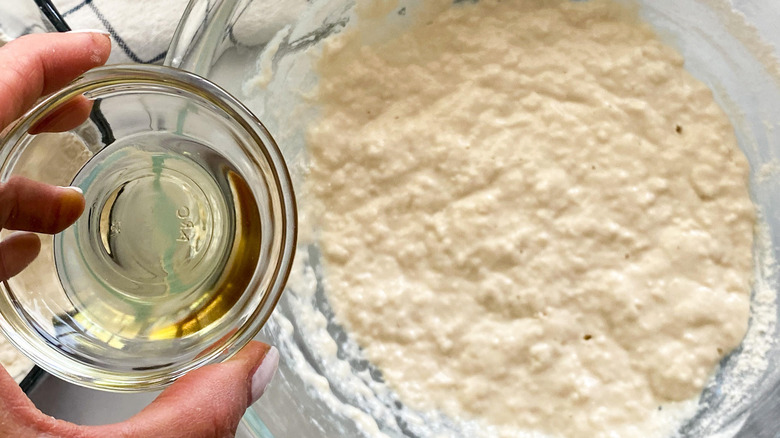 hand adding oil to bowl of dough