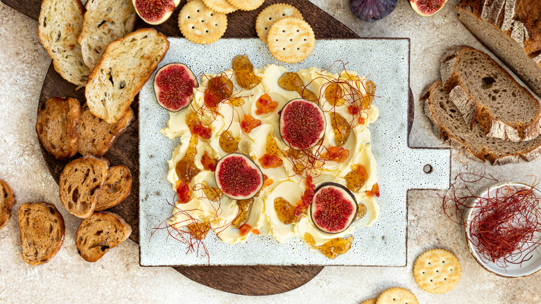 butter board with figs, honey, and brown bread on beige background