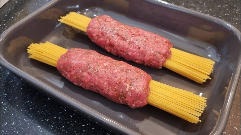 Raw ground beef wrapped around uncooked spaghetti