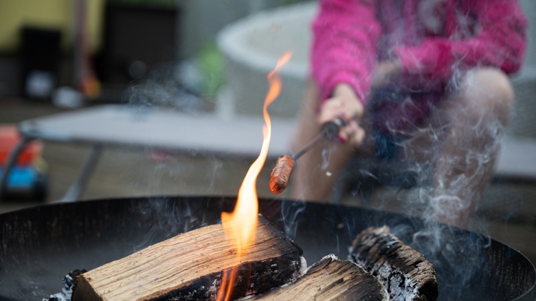 Woman cooks hot dog over open fire