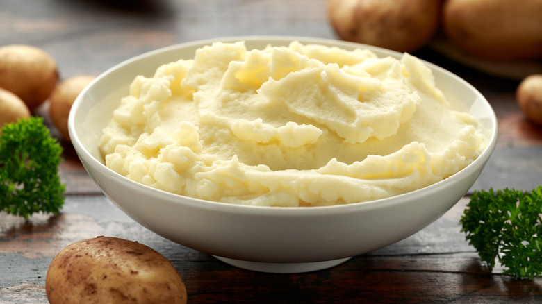 A bowl of creamy mashed potatoes with whole potatoes and garnish on the side