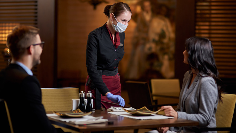 A couple dining at a restaurant with a masked server