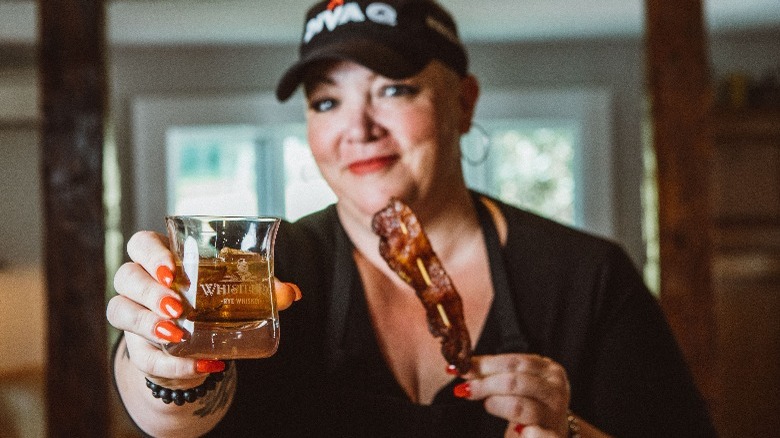 Diva Q holding glass of whiskey and bacon