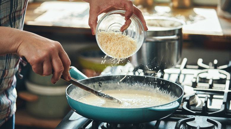 adding cheese to Alfredo sauce