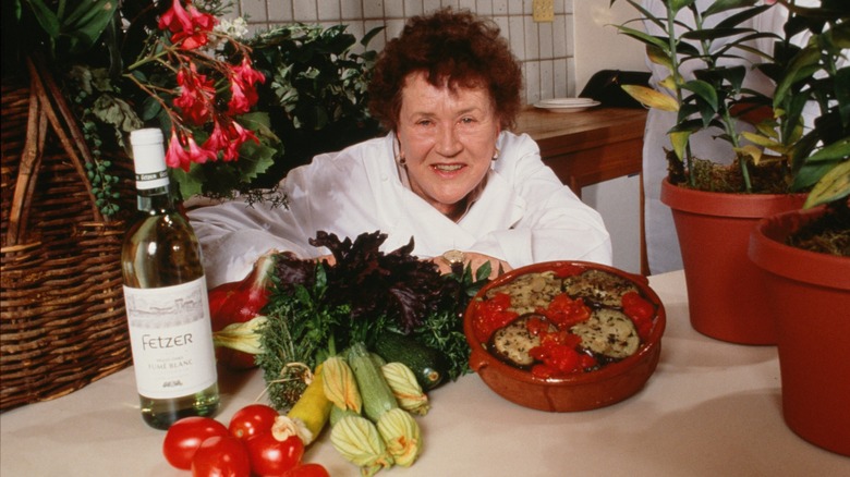 Julia Child smiles with food on a table