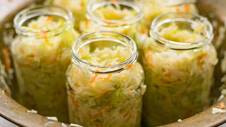 multiple opened glass jars of sauerkraut in large ceramic bowl