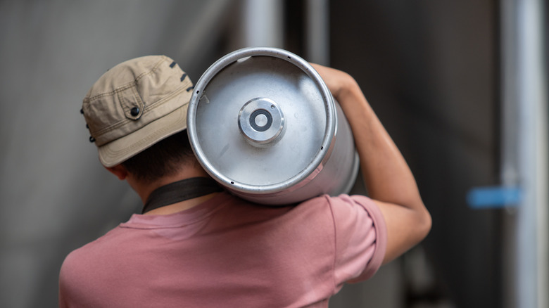 man in a baseball cap carrying a pony keg of beer