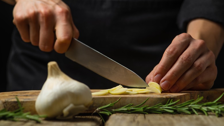 a man's hands chopping garlic on a wooden cutting board with rosemary in the foreground