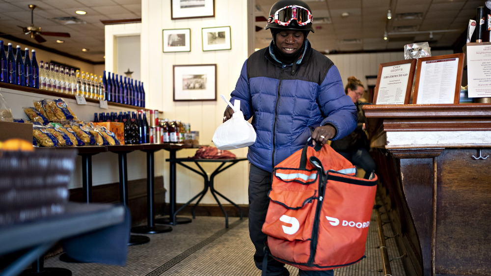 DoorDash delivery driver with bike helmet and delivery bag in restaurant picking up order