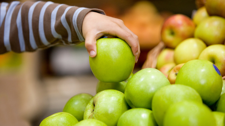 Hand selects a green apple from a pile