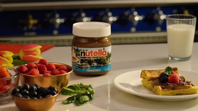 A jar of Nutella on a table with fruits 