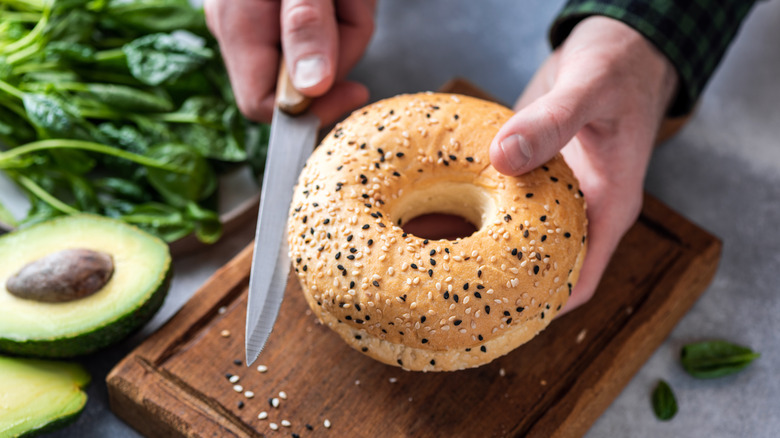 Person cutting bagel next to avocado