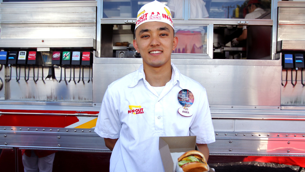 A smiling In-N-Out employee holding out a burger