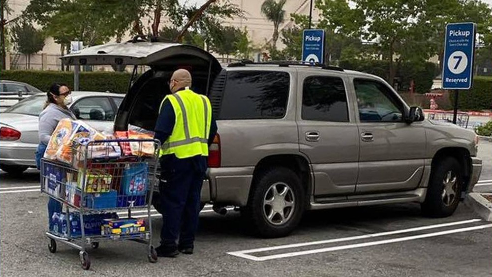 Sam's Club employee helping talking to customer outside of SUV with shopping cart full of items