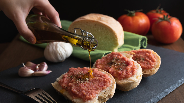 bread with tomato and hand drizzling olive oil