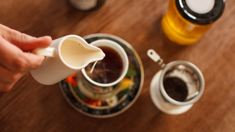 Person pouring milk into tea